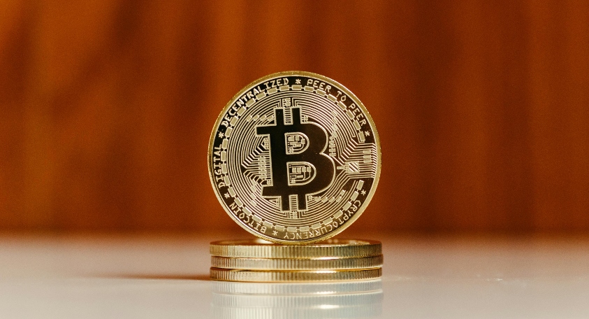 A golden Bitcoin standing on a stack of similar coins against a wooden background, symbolizing cryptocurrency and blockchain technology.