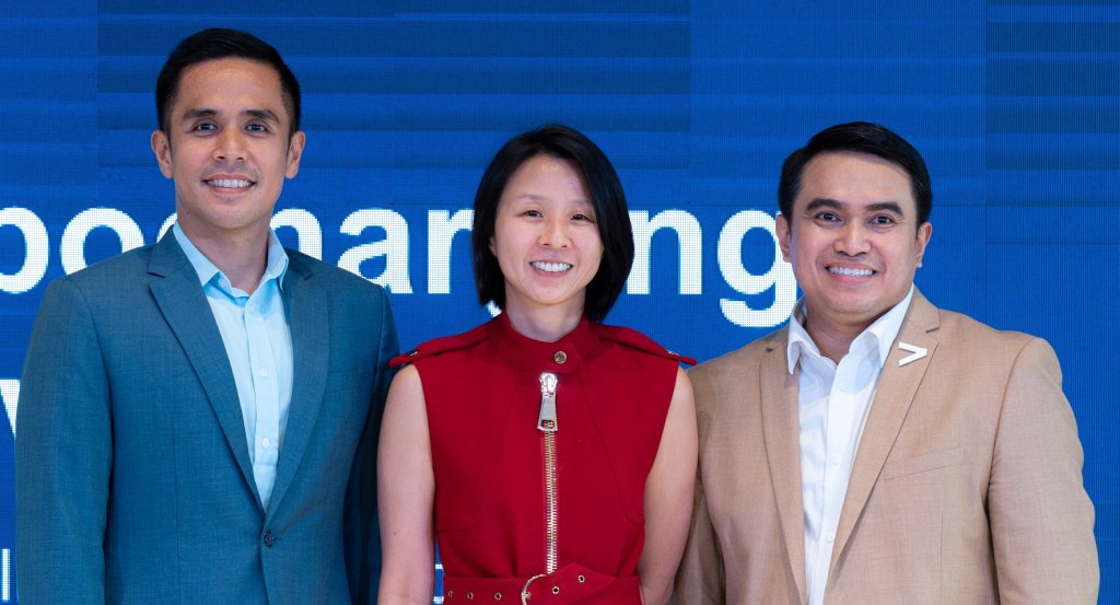 Three professionals pose together in front of a display screen at an event, showcasing teamwork and collaboration.