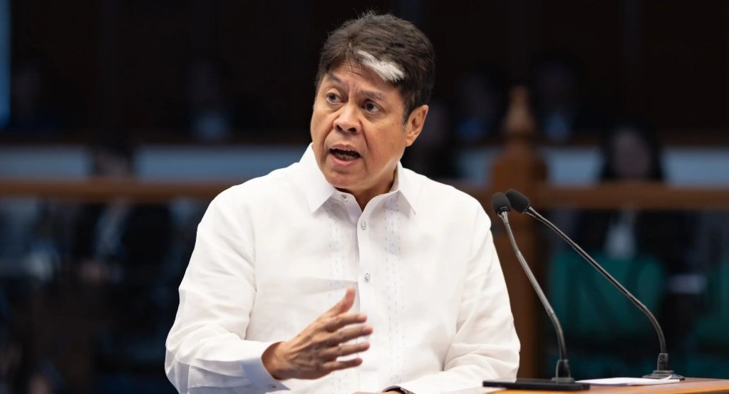 A man in a formal white barong speaks passionately at a podium, gesturing with his hand, in a legislative setting.