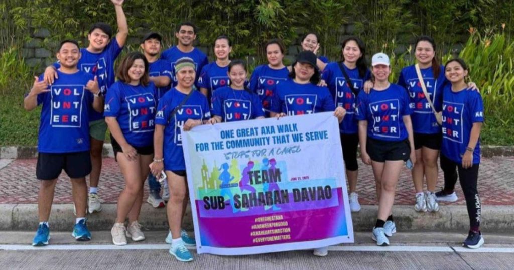 Group of AXA employees participating in the 'One Great AXA Walk' event, wearing blue volunteer shirts and holding a banner in Davao, Philippines.