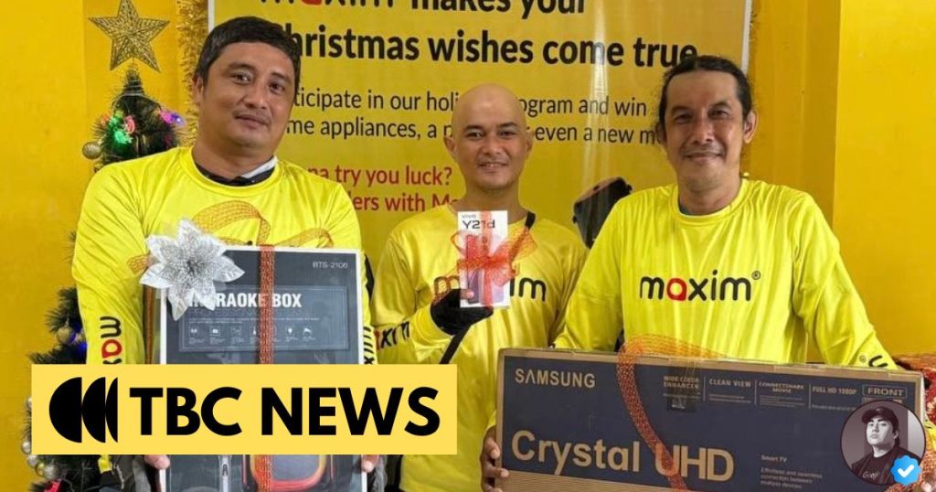 Three men in yellow t-shirts holding prizes, including a karaoke box and a Samsung TV, in a festive setting with a holiday banner in the background.