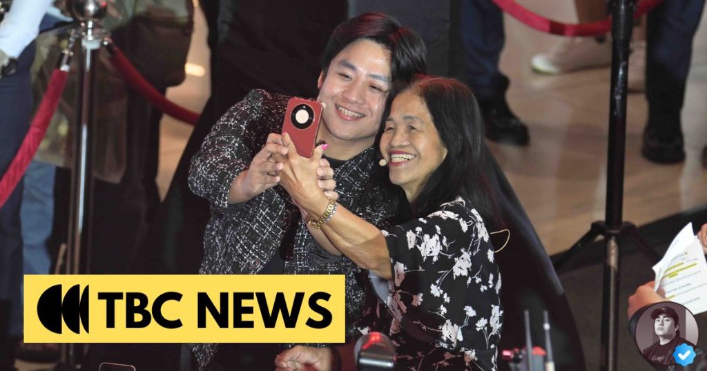 Two individuals happily taking a selfie together at a public event, with a TBC News logo displayed prominently in the foreground.
