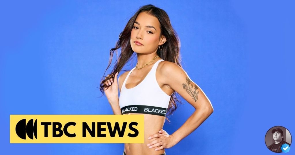 A young woman posing confidently in a white crop top with a black band, against a solid blue background. The image features a logo for 'TBC News' at the bottom left corner.