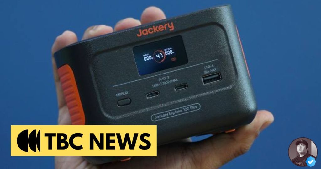 A person holding a Jackery Explorer 100 Plus portable power station with a digital display, showing input and output options including USB ports, against a blue background.