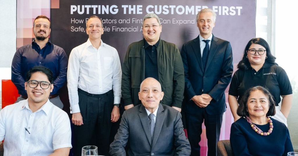 Group photo of a diverse team of professionals in a business setting, standing and sitting in front of a backdrop that reads 'Putting the Customer First'.