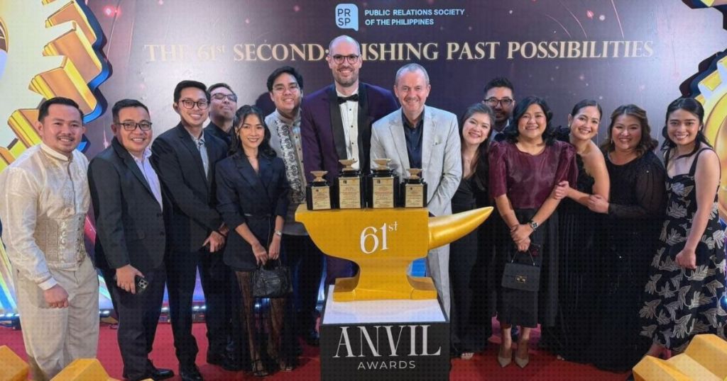 Group of people posing at an awards ceremony, standing in front of a large golden anvil trophy with the text '61st ANVIL AWARDS' and 'Publishing Past Possibilities' in the background.