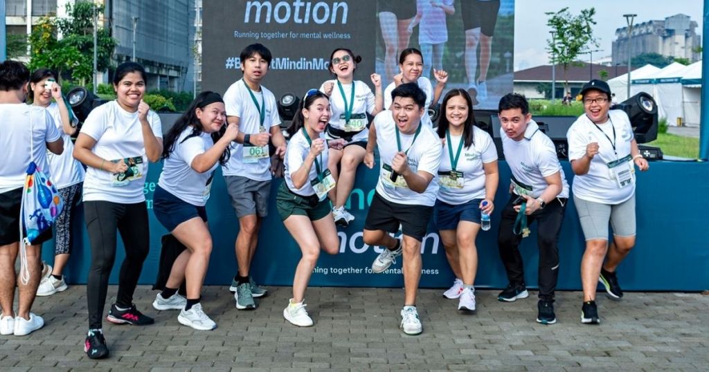 Group of people in white shirts participating in a wellness event, striking cheerful poses in front of a promotional backdrop.