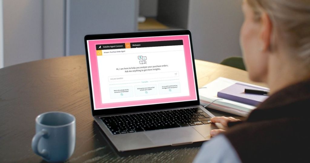 A person sitting at a table working on a laptop displaying a customer support interface for analyzing purchase orders, with a coffee mug and stationery in the foreground.