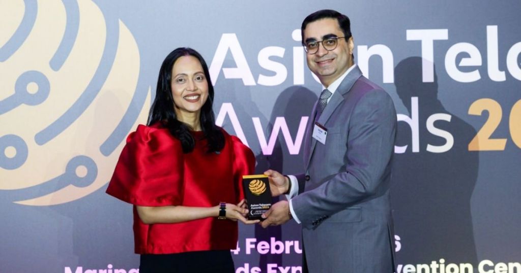 Two individuals at the Asian Telecom Awards, one in a red dress and the other in a grey suit, presenting an award with a backdrop featuring the event's logo.