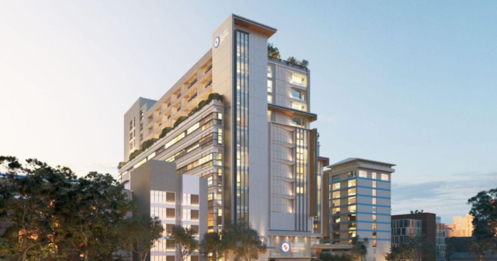 Modern multi-story building with large glass windows and balconies, surrounded by trees and a clear sky.