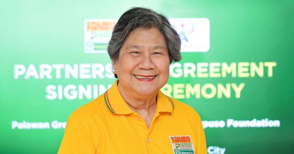 A smiling woman wearing a bright yellow shirt, standing in front of a green backdrop with text that reads 'PARTNERSHIP SIGNING CEREMONY' and logos for the Palawan Green House Foundation.