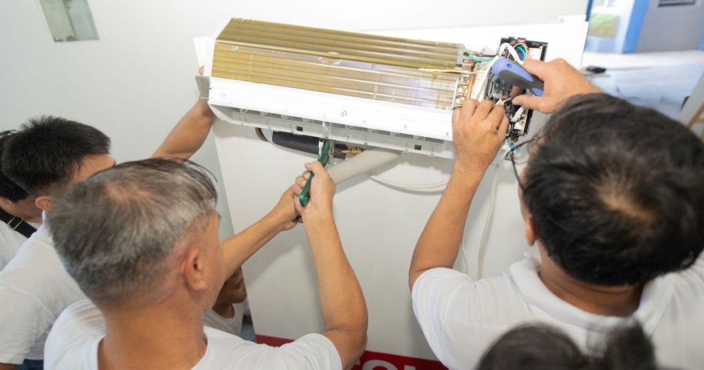 A group of technicians collaboratively working on the components of an air conditioning unit, with tools in hand and parts being examined.