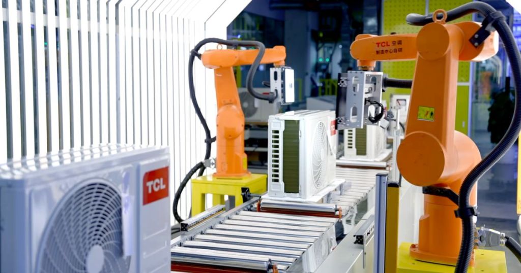 Industrial robotic arms assembling air conditioning units on a conveyor belt in a modern manufacturing facility.