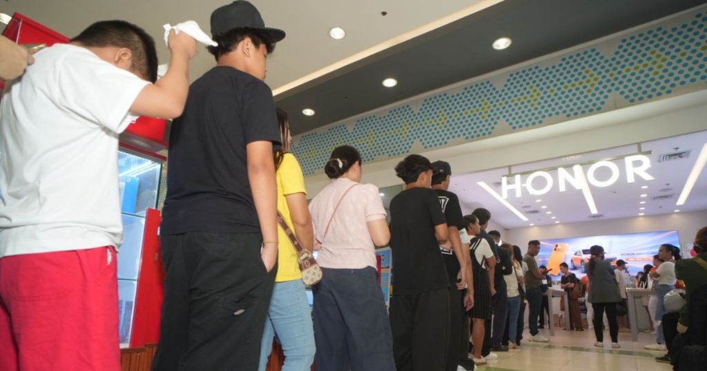A line of people waiting inside a store with a prominent 'HONOR' sign in the background, showcasing a retail environment.