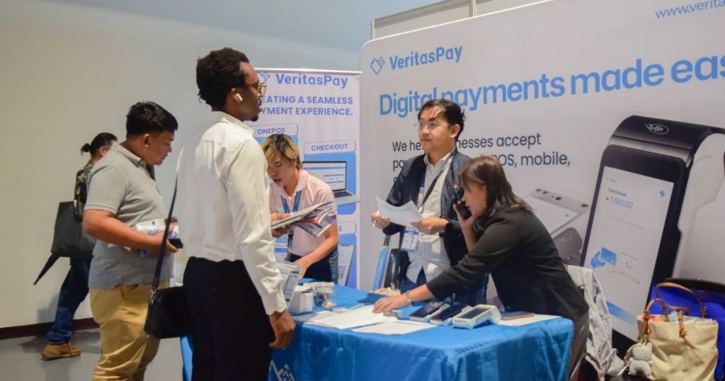 A group of people engaging at a VeritasPay booth showcasing digital payment solutions, with informational materials and devices on a table.