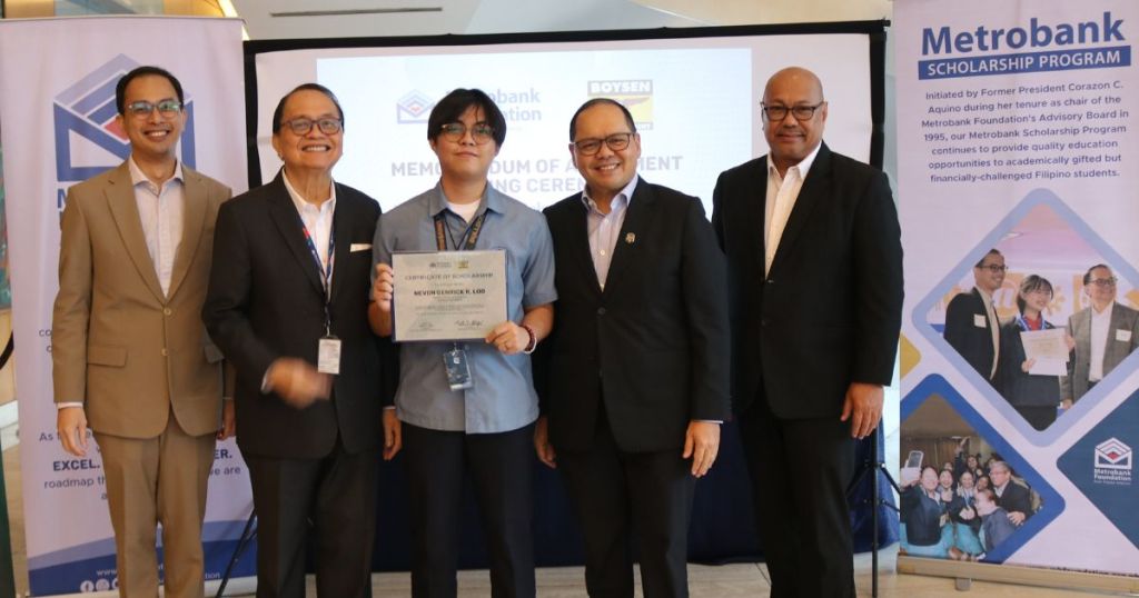 Group photo of six individuals at a Metrobank Scholarship Program event, with one student holding a certificate and various banners in the background.